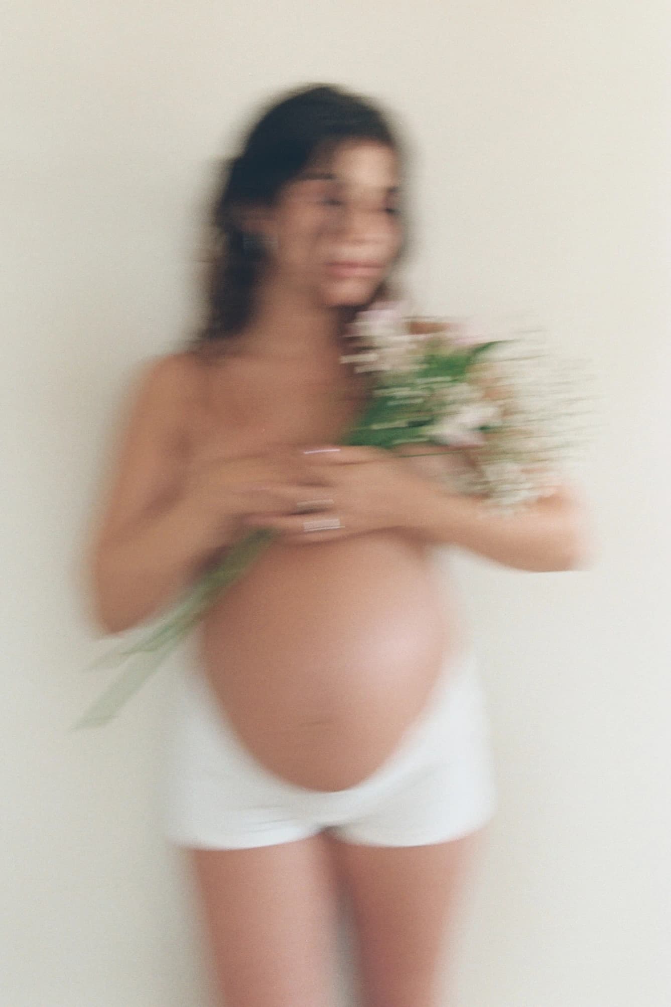 Mujer embarazada de pie sosteniendo un ramo de flores, con camiseta blanca.