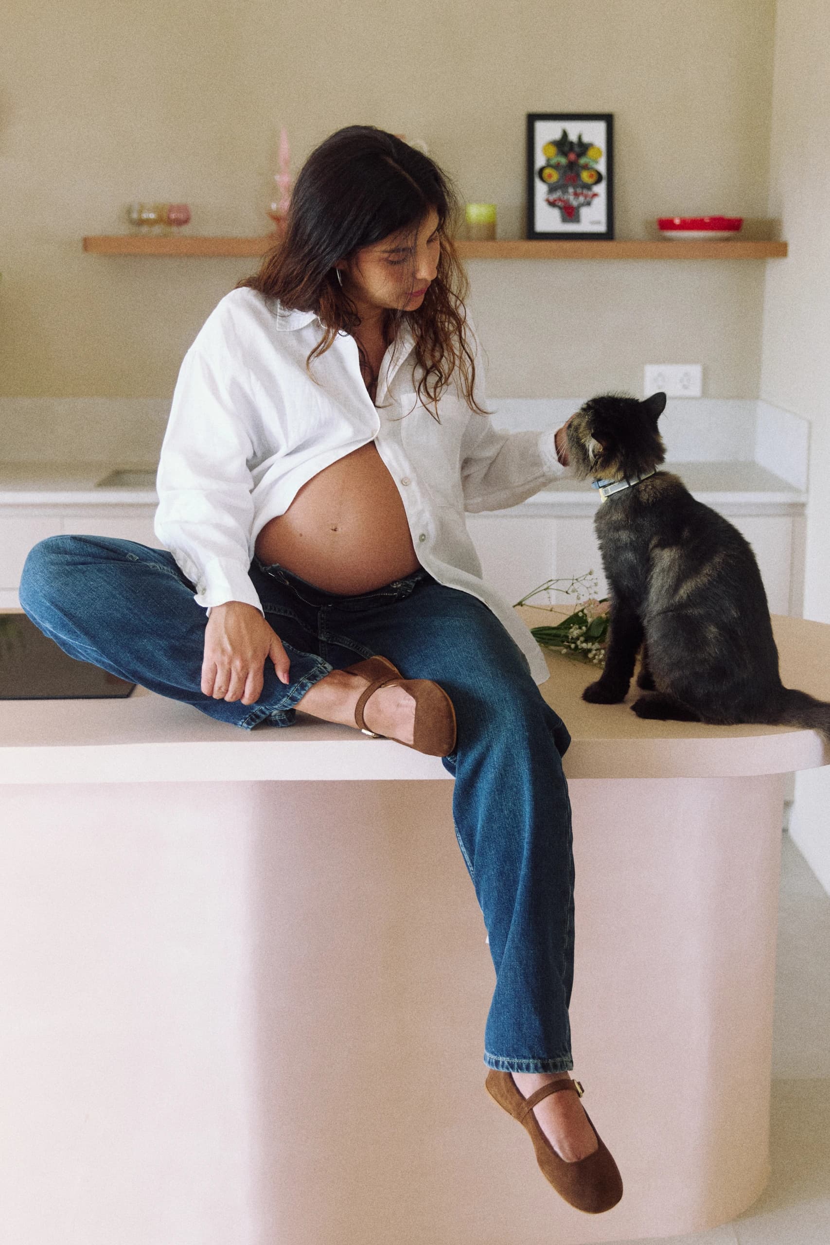 Mujer embarazada sentada junto a un gato mientras alguien la fotografía.