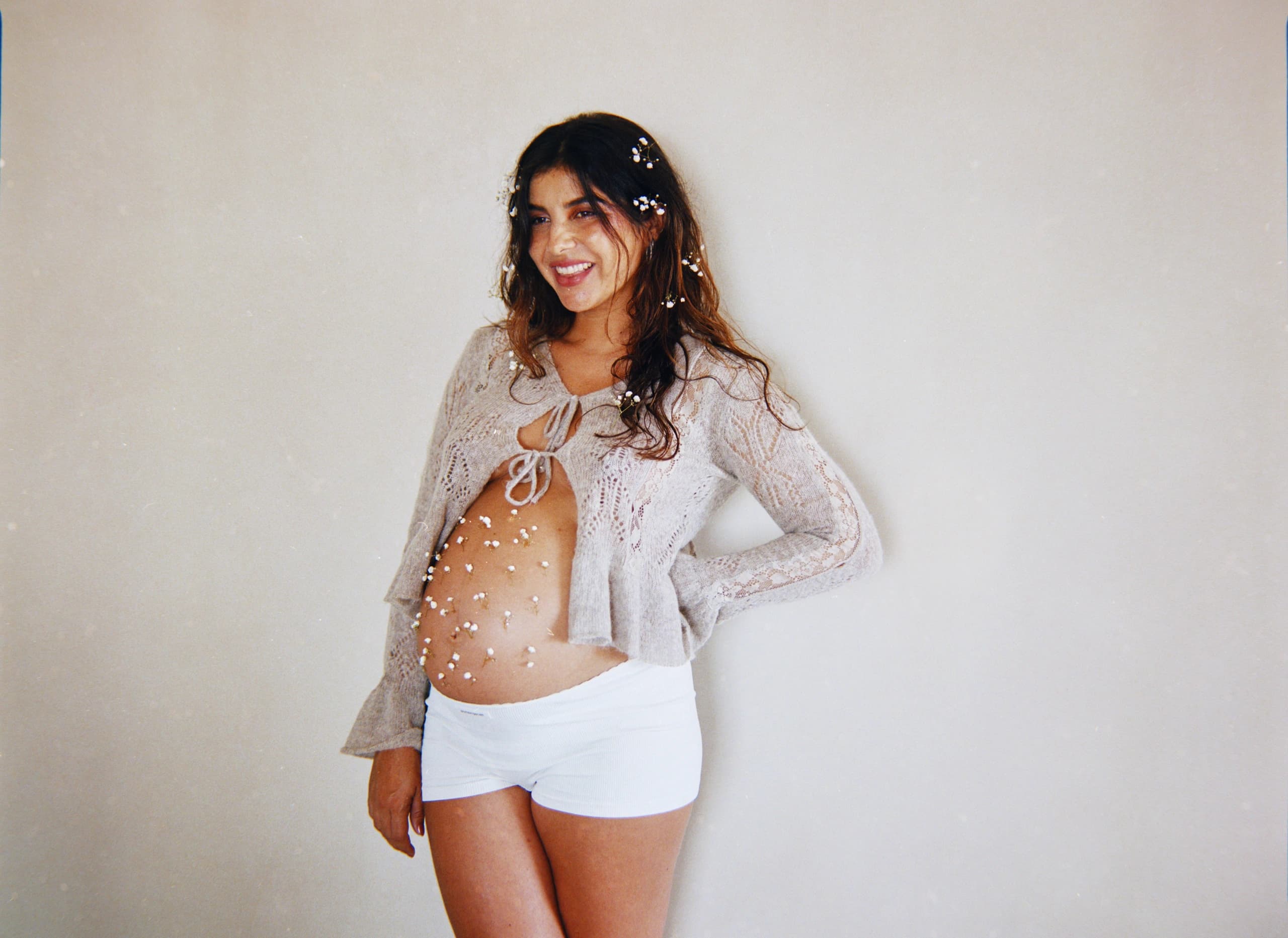 Mujer embarazada sonriendo con flores blancas sobre el abdomen.